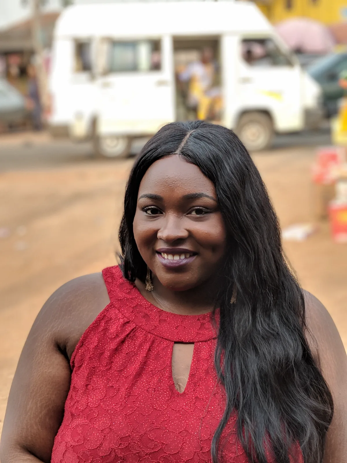 Chizo smiling in a red lace top on a street, a white bus behind her.