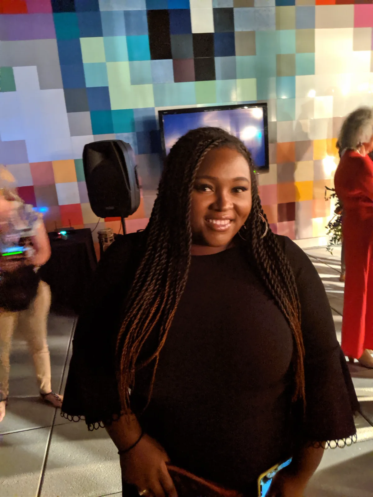 Chizo in a black top with long braids, in front of a wall of coloured tiles.