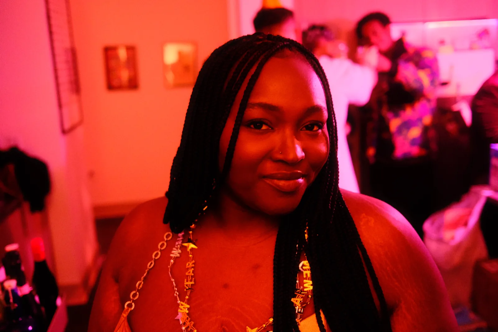 Chizo with braids, smiling in warm pink light at a gathering.