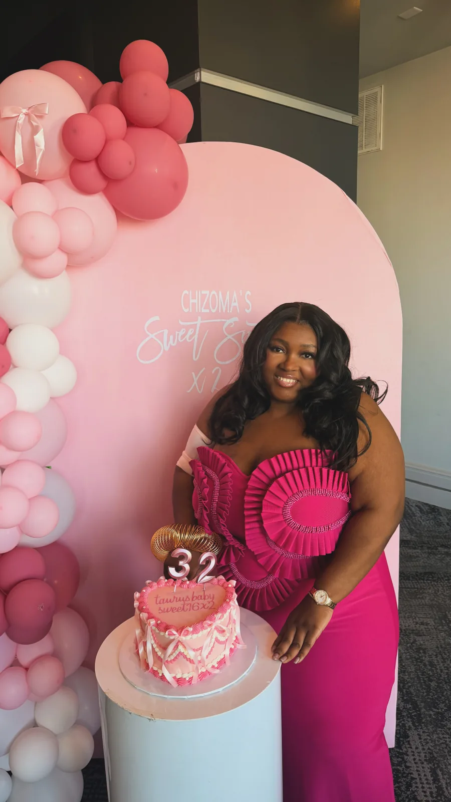 Chizo in a pink gown beside a birthday cake and pink balloons.