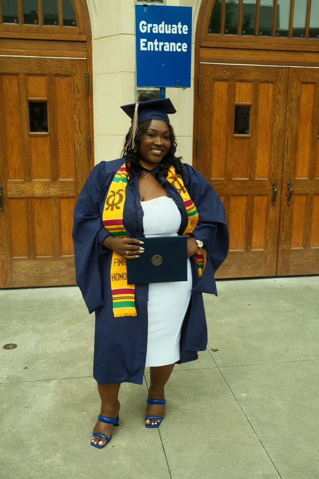 Chizo in a graduation gown, cap, and kente stole, holding her diploma.