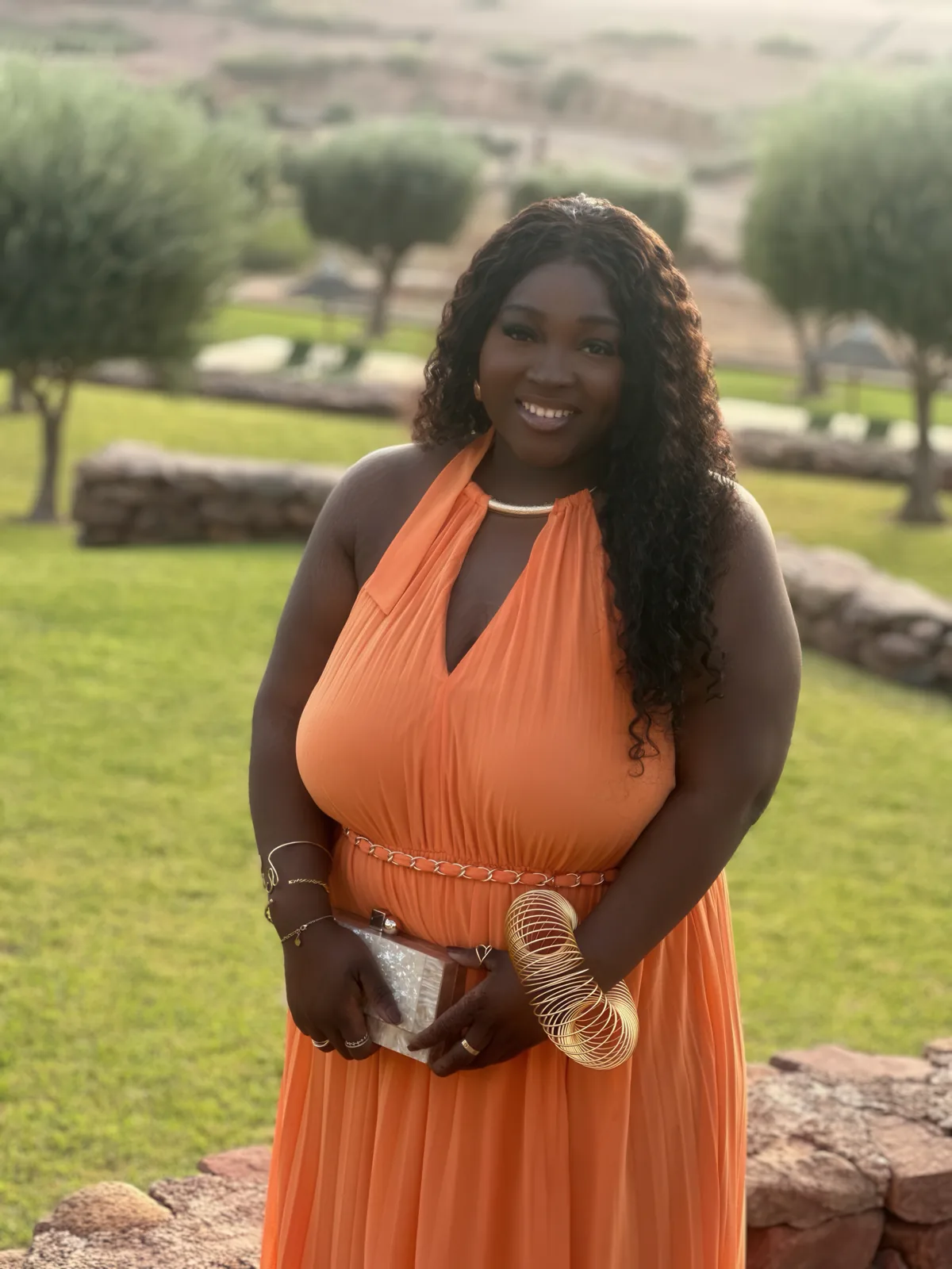 Chizo in an orange dress on a lawn, hills behind her in evening light.